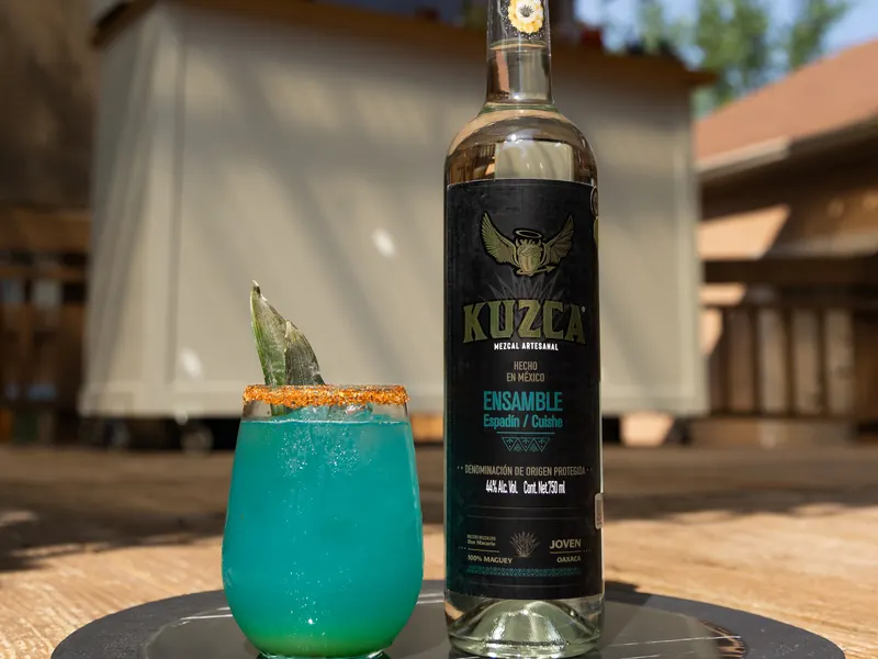 Mezcalita Indiferente bleue, verre givré, à côté d'une bouteille de Kuzca Ensamble